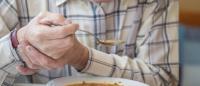 older man struggling to eat soup due to an essential tremor